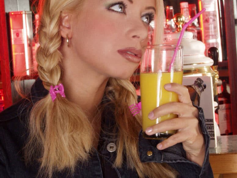 Blondine mit Zöpfen hält Cocktailglas in der Hand